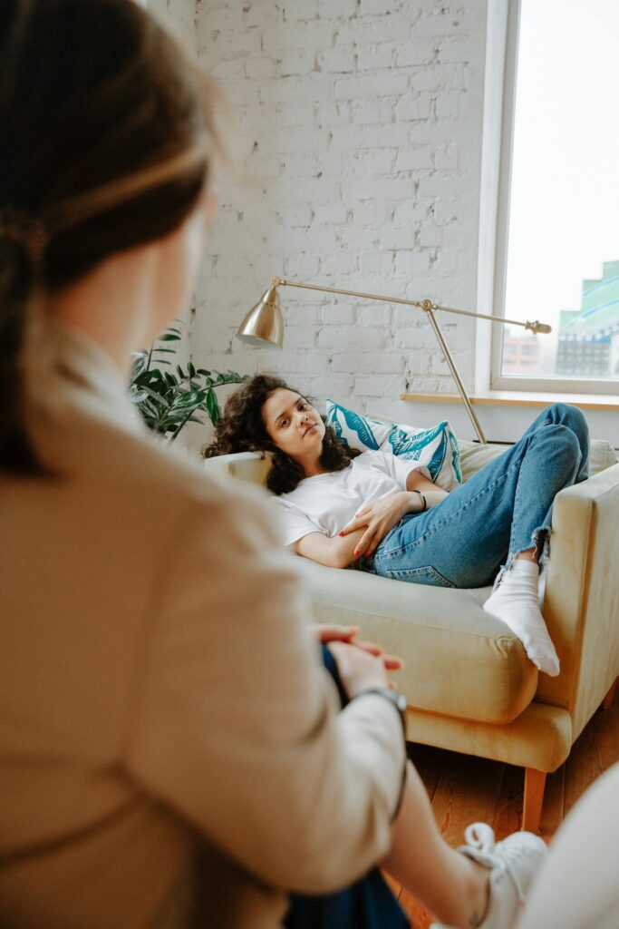 A young woman in a casual therapy session, relaxing on a sofa, while a coach listens attentively.